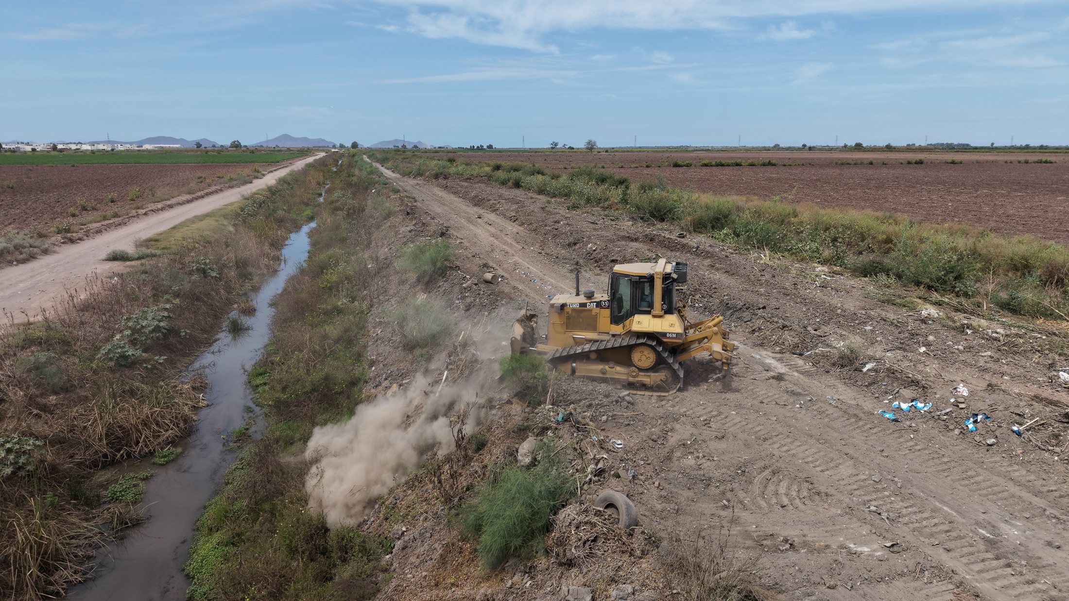 Canal y camino de servicio. Toma aérea de campo abierto con maquinaria sobre el bordo operativo.